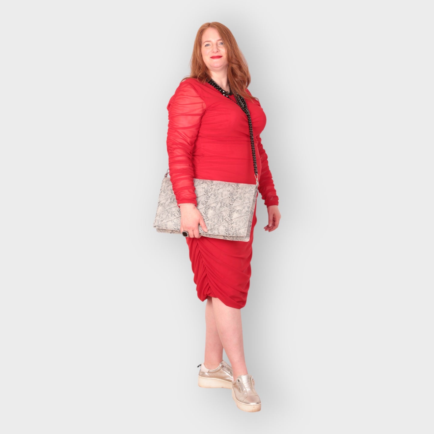 Woman in a red outfit holding a snakeskin quilted laptop clutch bag against a white background