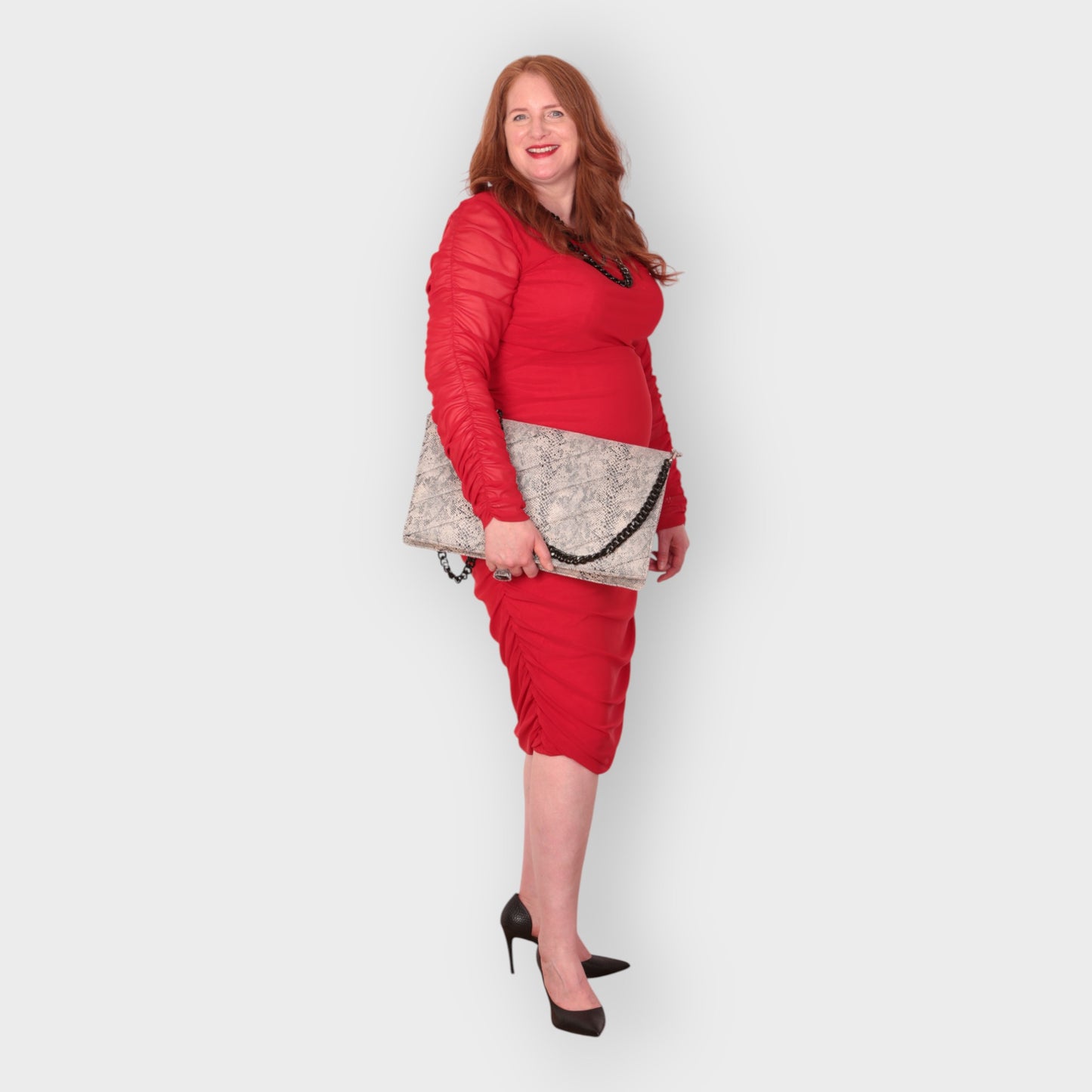 Woman in a red outfit holding a snakeskin quilted laptop clutch bag against a white background