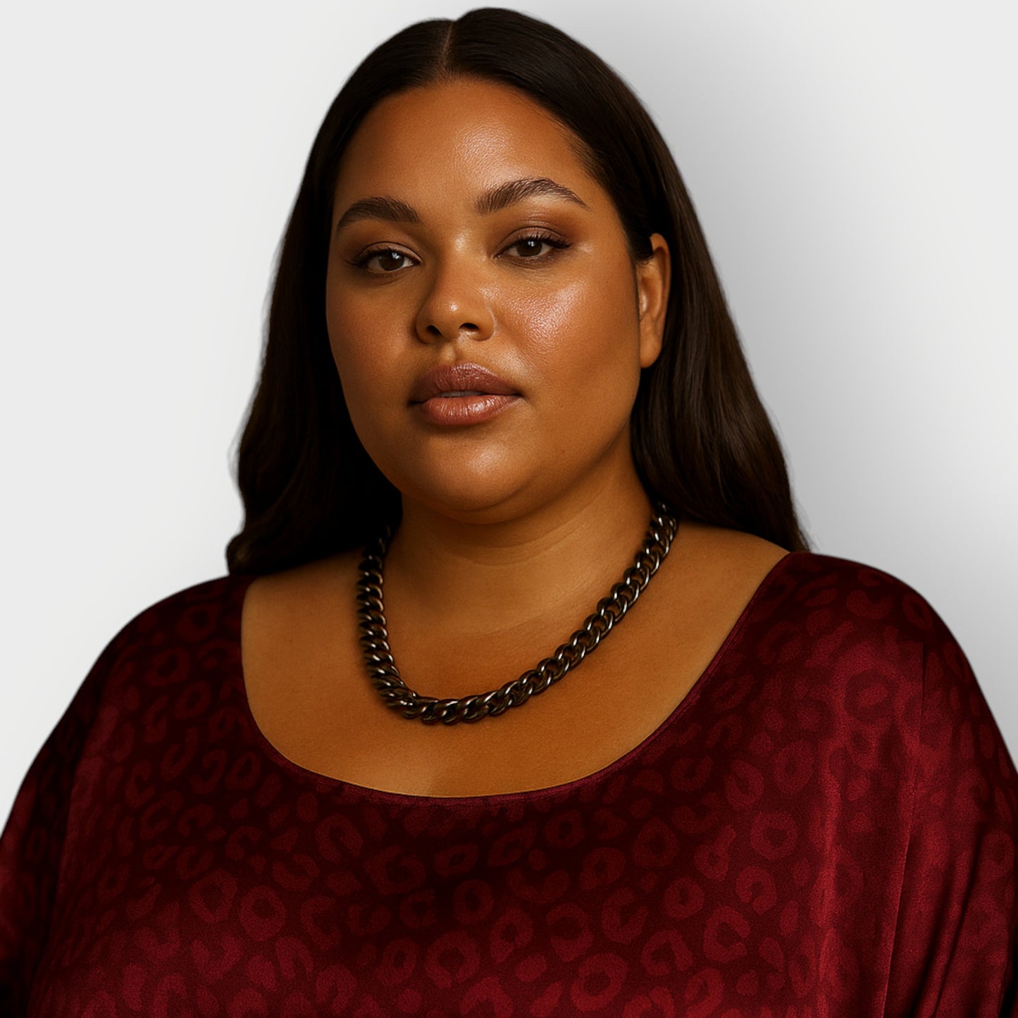 Woman wearing a burgundy dress and a single tier black aluminium chain necklace a against a plain background