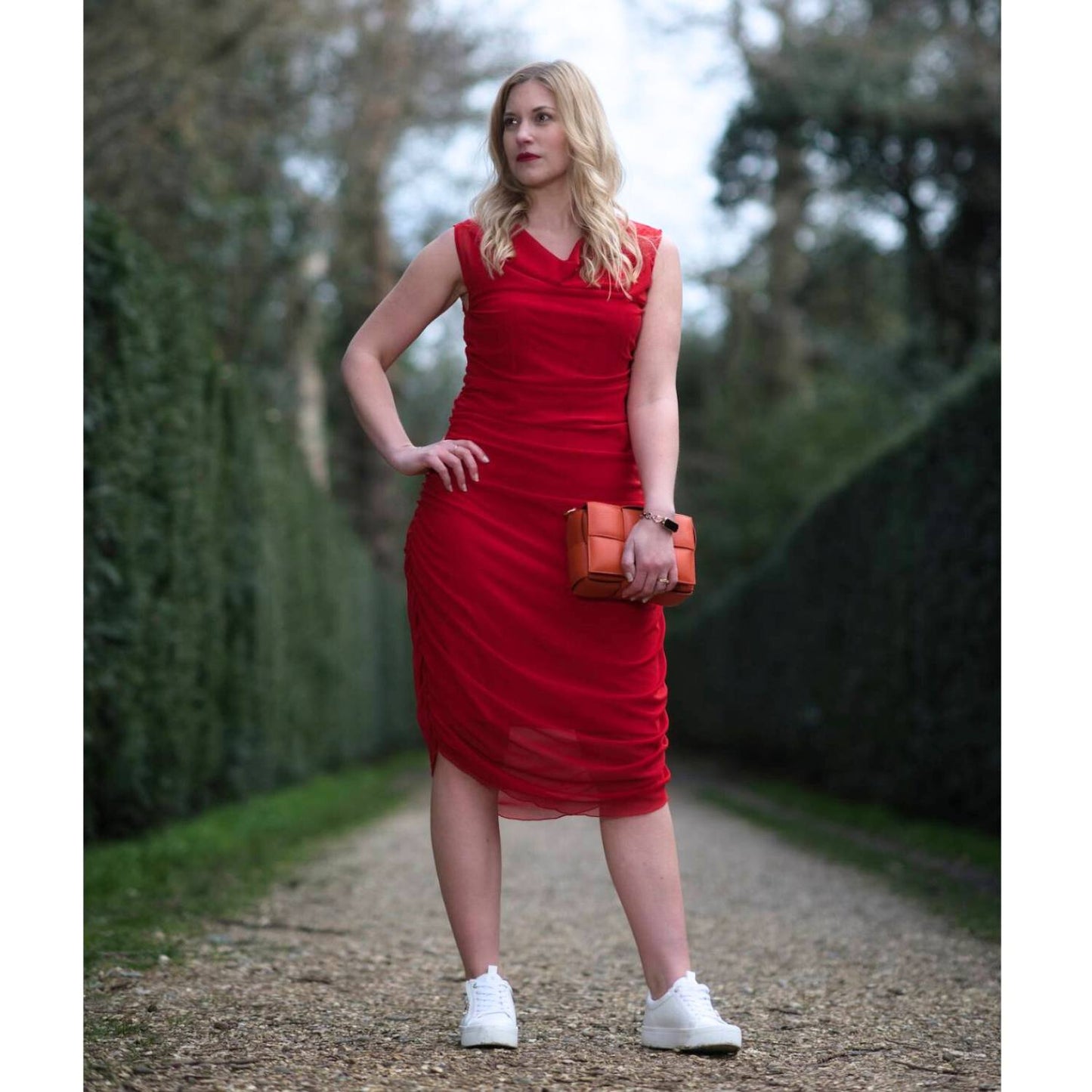 Women's Boudicca Summer Red Ruched Bodycon Midi Dress styled with an orange handbag and white sneakers for a chic, modern ensemble.