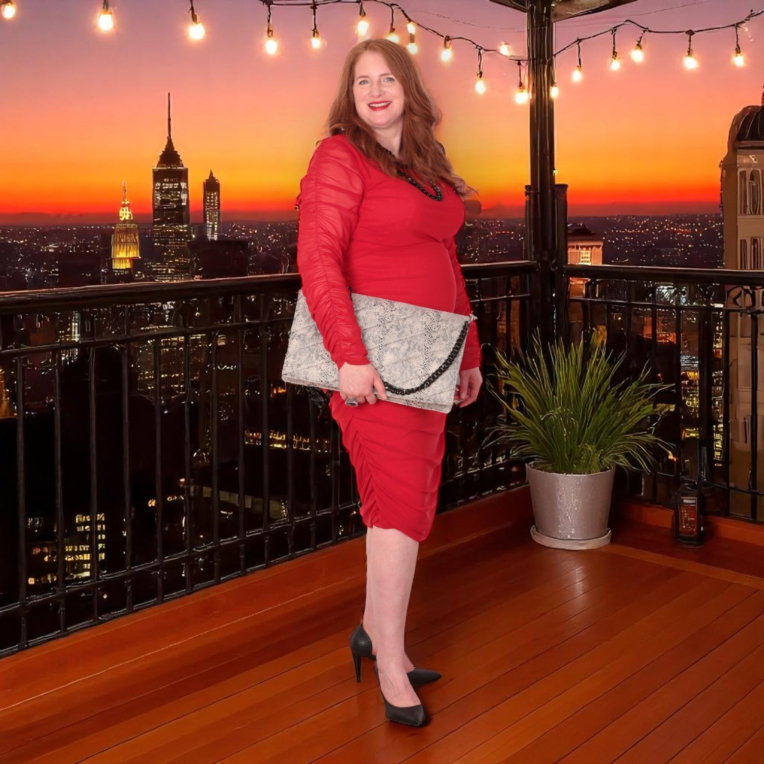 Woman in a red outfit holding a snakeskin quilted laptop clutch bag  in a red outfit standing on a rooftop with a cityscape and sunset in the background