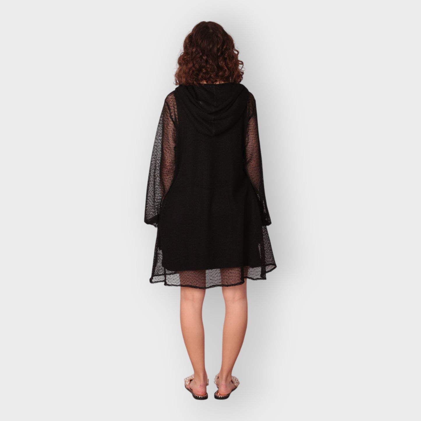 Person wearing a black dress with sheer sleeves, hoodie and black undergarment on a white background. photographed from the back