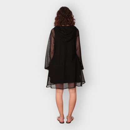 Person wearing a black dress with sheer sleeves, hoodie and black undergarment on a white background. photographed from the back