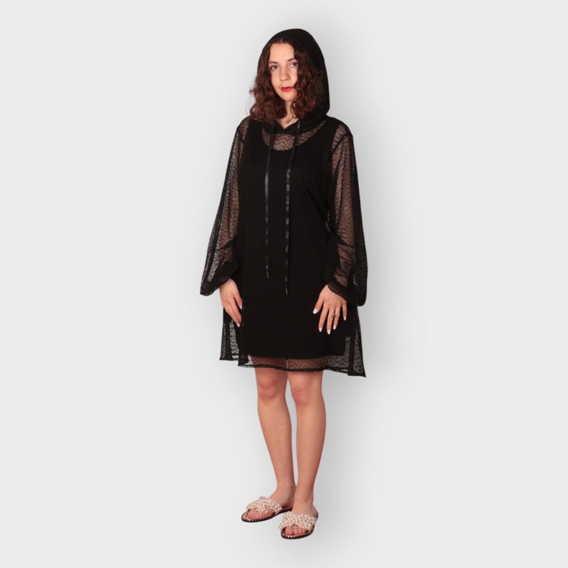 Woman wearing a black dress with sheer sleeves , hoodie and black undergarment against a white background