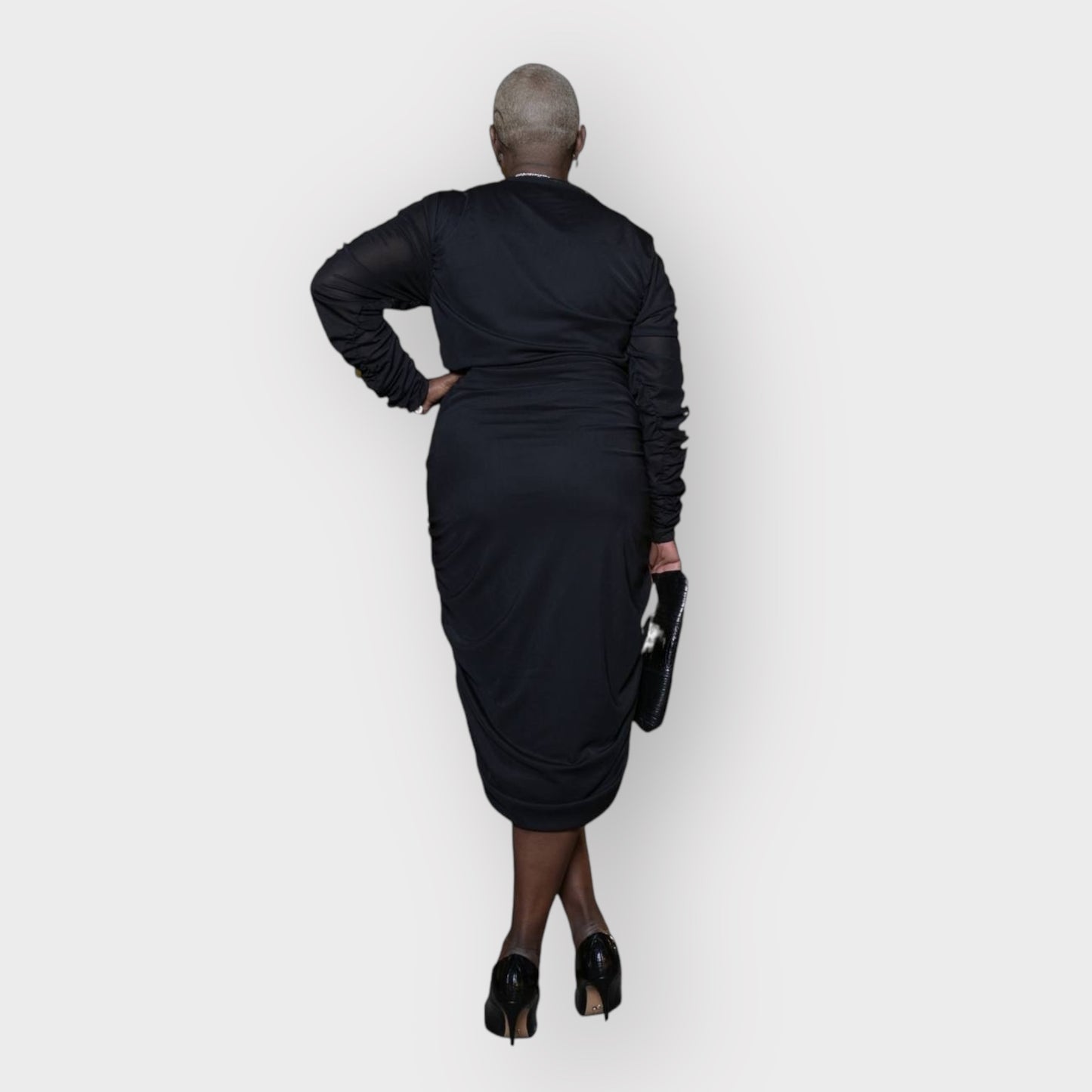 Plus-size woman wearing a black Boudicca Ruched Bodycon Midi Dress, styled with black heels. White Background.