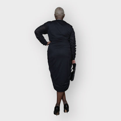 Plus-size woman wearing a black Boudicca Ruched Bodycon Midi Dress, styled with black heels. White Background.