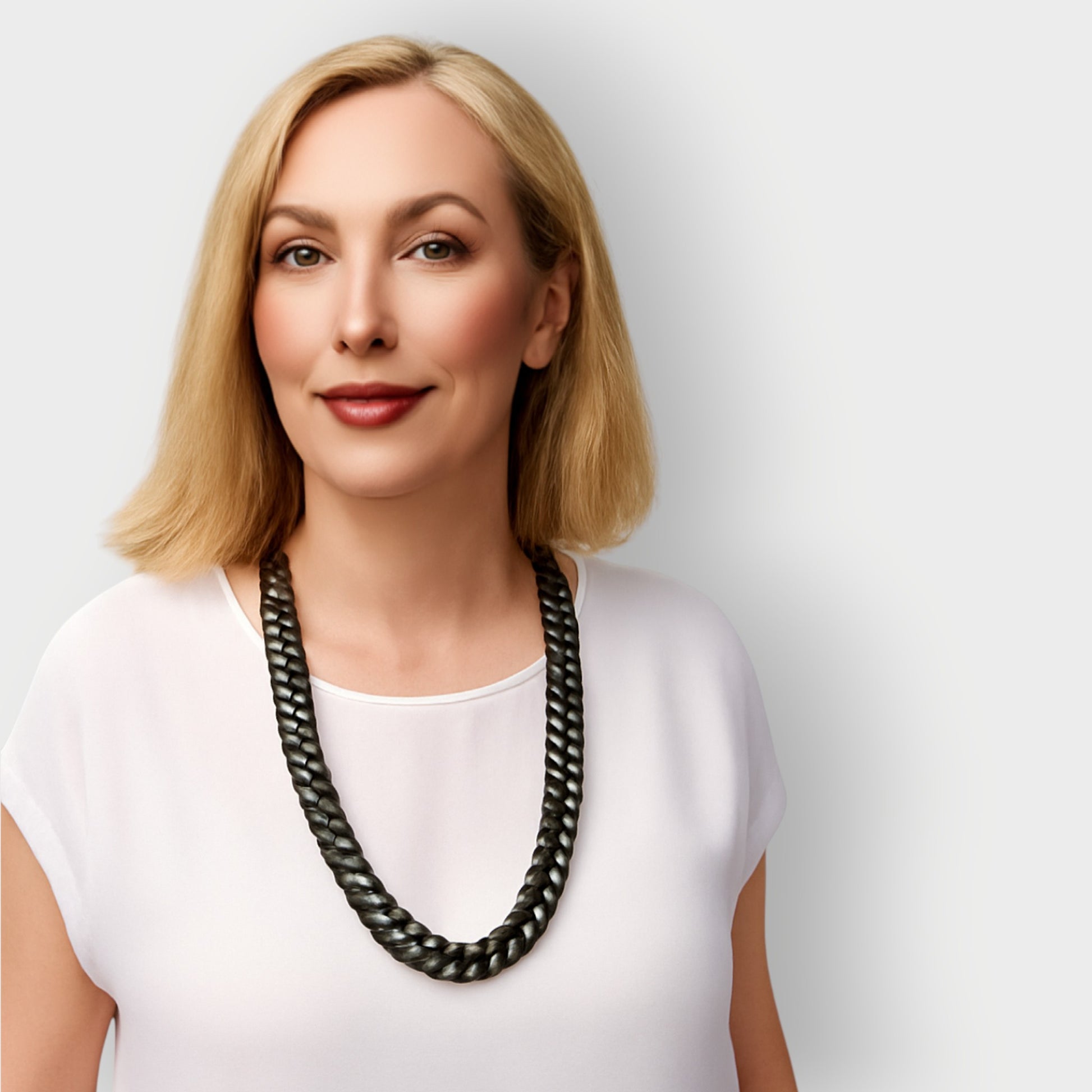 Woman wearing sunglasses and a long black aluminium single tier necklace against a plain background