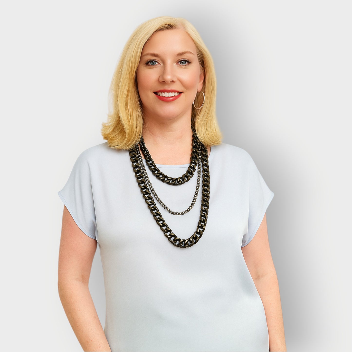 Woman wearing a white top and a tree tiered black aluminium and metal chain necklace a against a plain  background