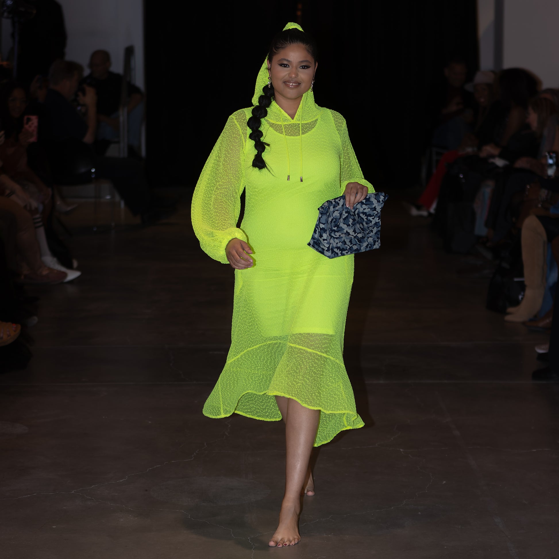 Model wearing a bright green dress on a runway with a dark background