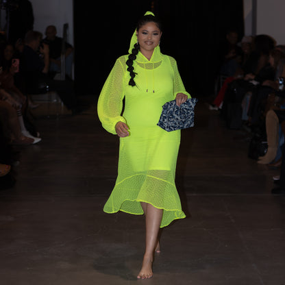 Model wearing a bright green dress on a runway with a dark background