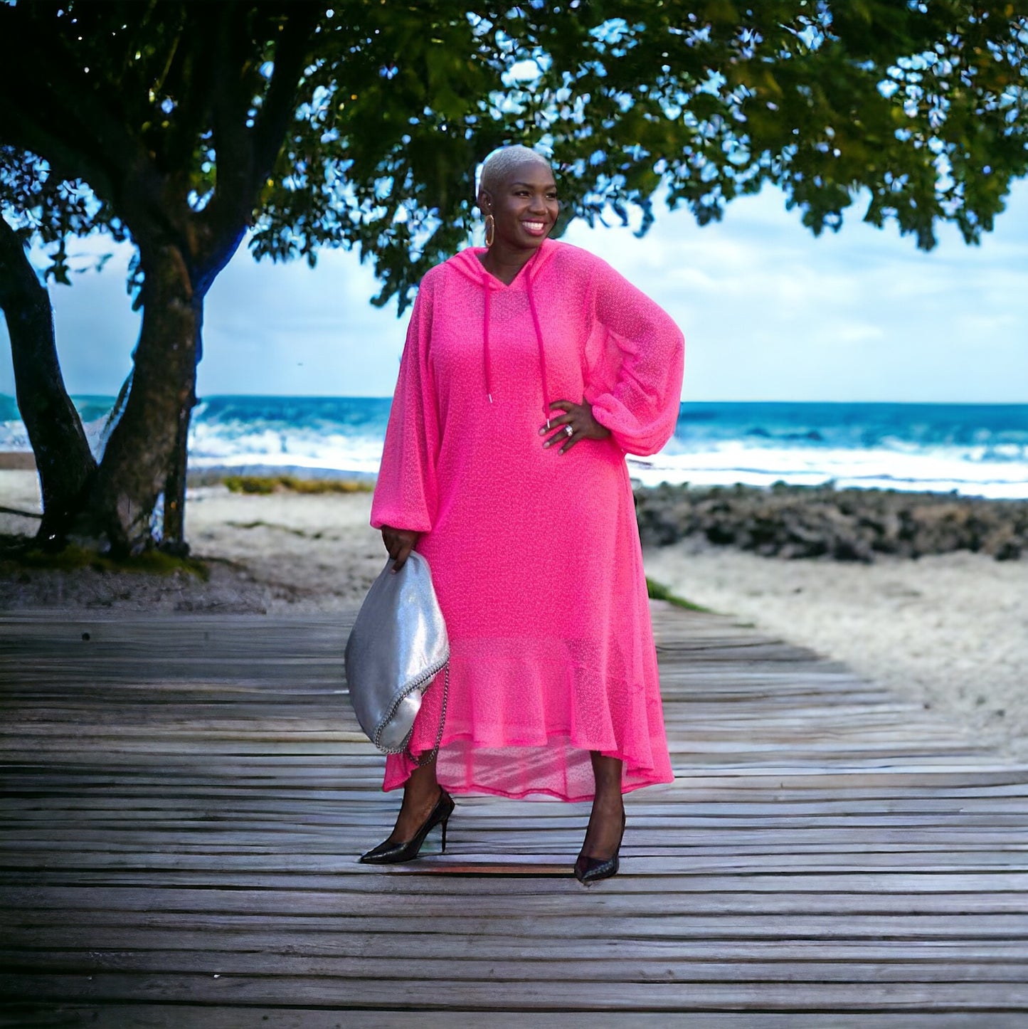 Women's Plus Size Aphrodite Hot Pink Holiday Resort Dress with hoodie and hot pink undergarment, paired with a silver handbag and black heels for a chic beach look.