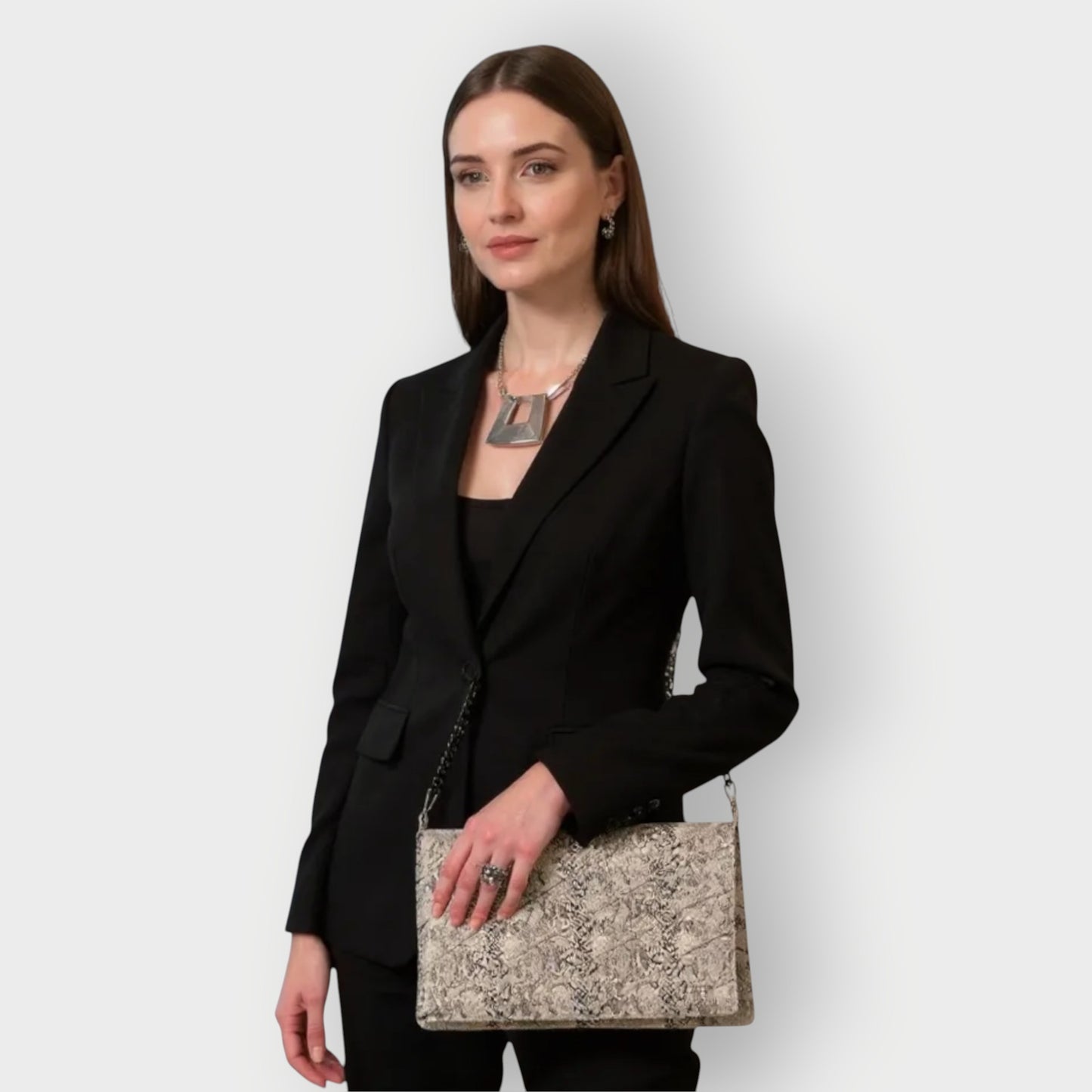 Woman in a black blazer holding a white black snakeskin clutch handbag against a white background