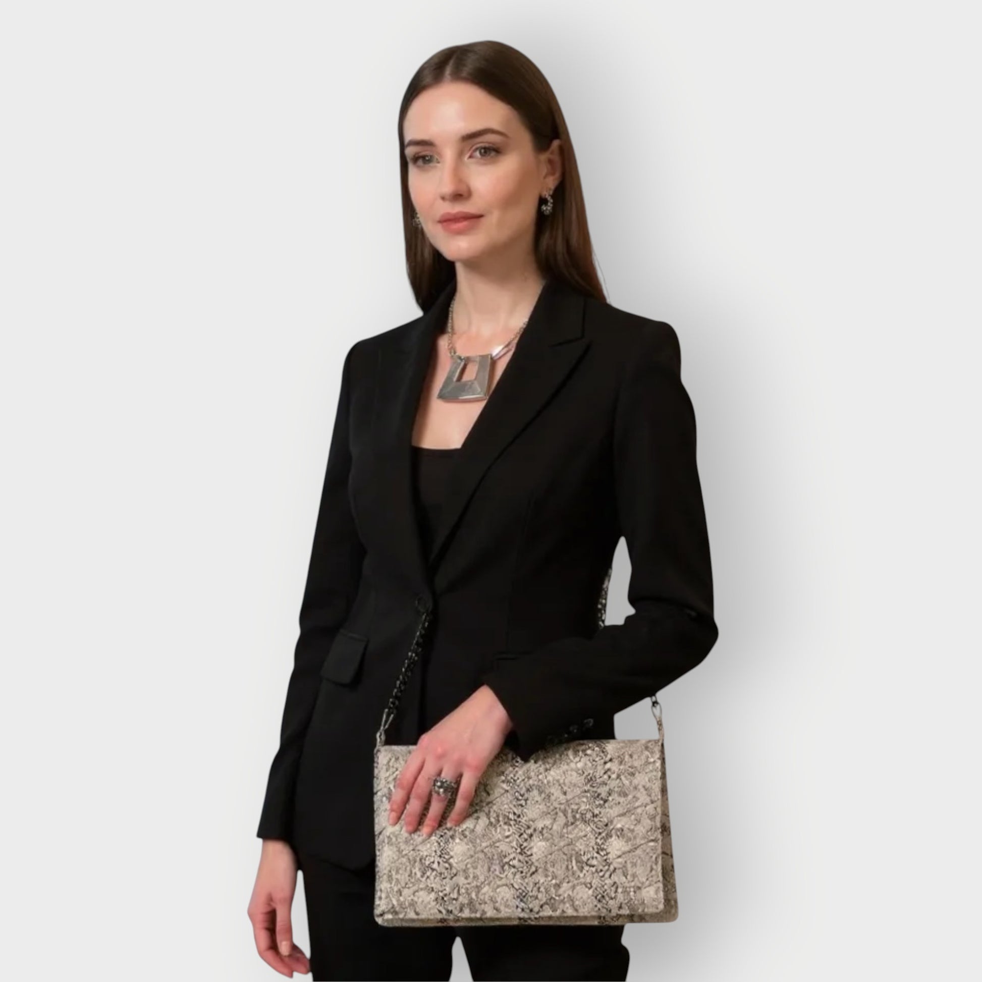 Woman in a black blazer holding a white black snakeskin clutch handbag against a white background