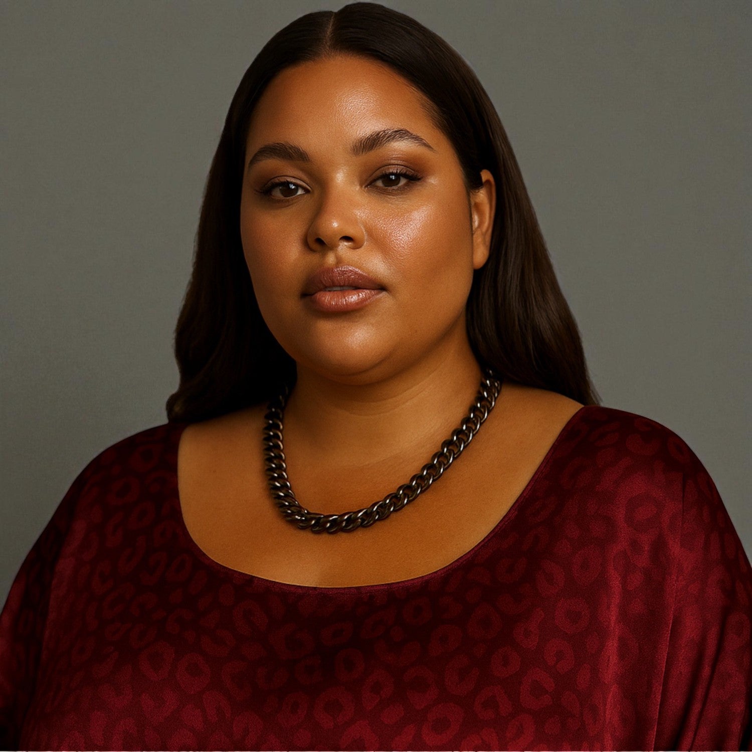 Woman wearing a burgundy dress and a single tier black aluminium chain necklace a against a plain  background