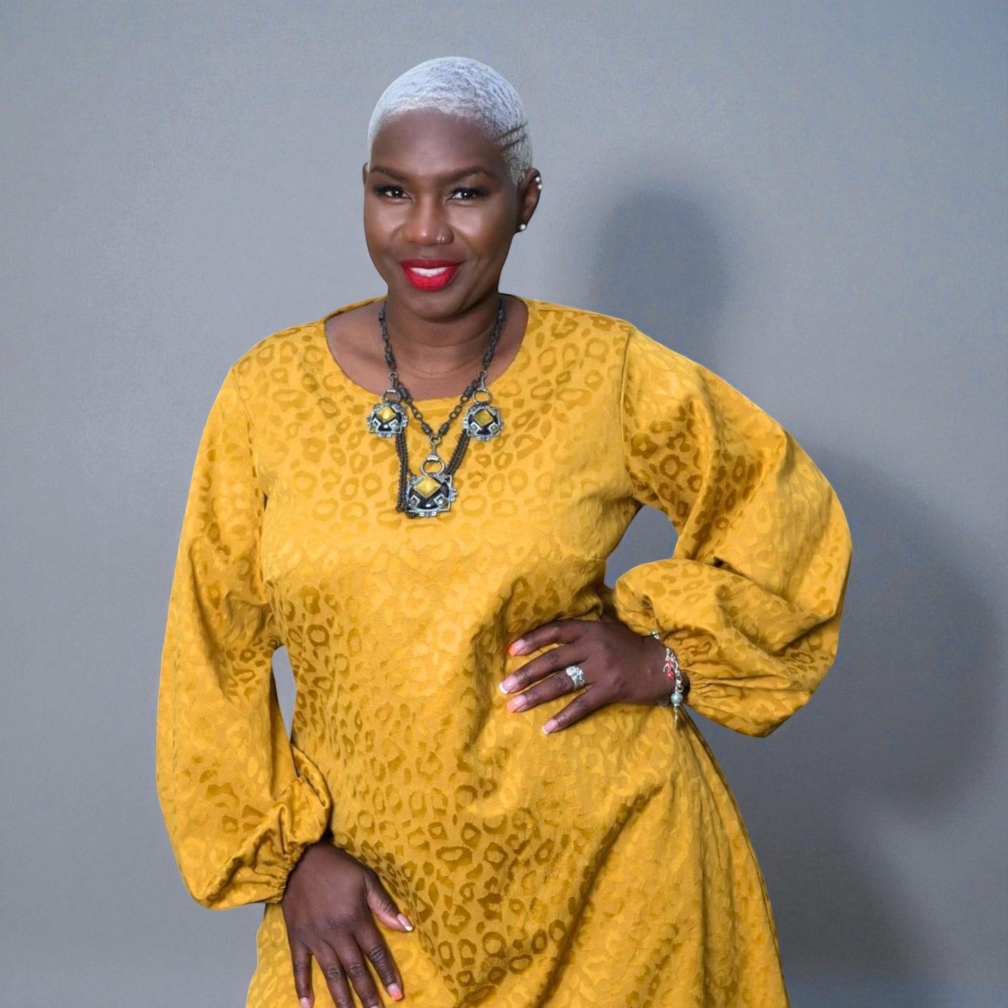 Women's Plus Size Gold Aphrodite Leopard Jacquard Dress shown as a close up, styled with a yellow stone necklace for an elegant look. Gray Background.