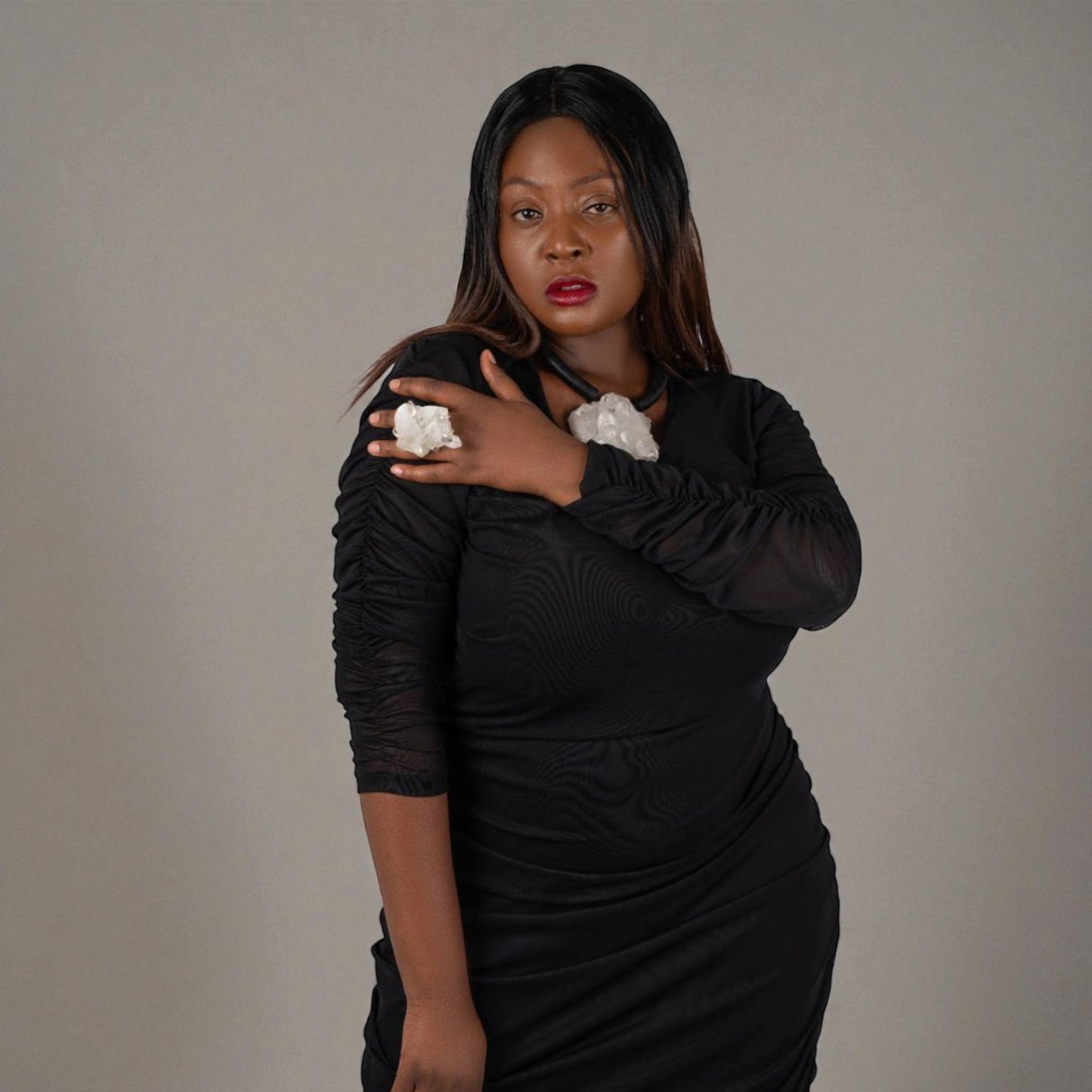 Plus Size Woman wearing a black ruched midi dress with quartz jewellery by Veronique Designs on a gray background.