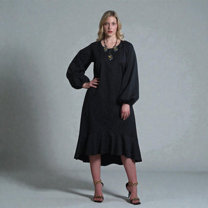 Women's Aphrodite Black Leopard Jacquard Dress styled with a gold necklace, black clutch and gold chain heels for a chic, coordinated look. Gray background.