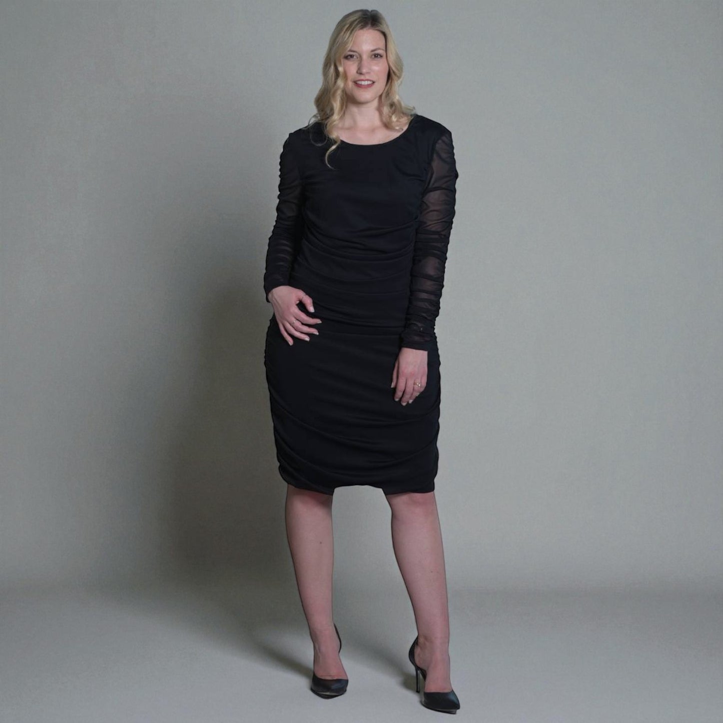 Women's Black Mid Size Ruched Bodycon Midi Dress styled with black heels for a classic and elegant touch. Plain background.