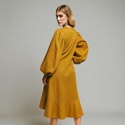 Woman wearing a mustard yellow dress with puff sleeves on a plain background