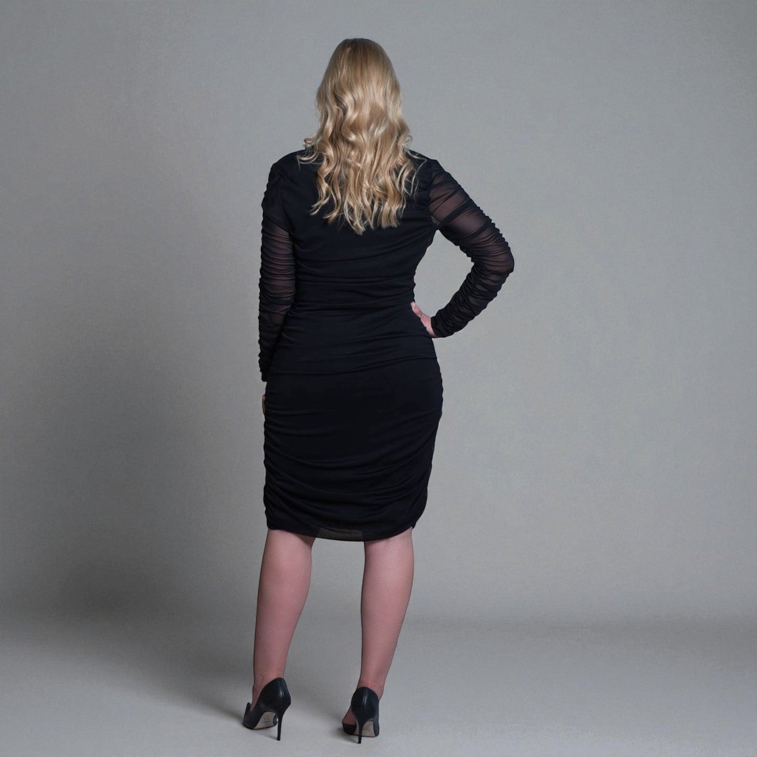 Women's Black Mid Size Ruched Bodycon Midi Dress styled with black heels for a classic and elegant touch. Plain background.