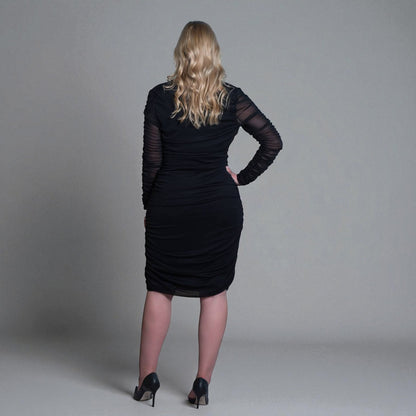 Women's Black Mid Size Ruched Bodycon Midi Dress styled with black heels for a classic and elegant touch. Plain background.