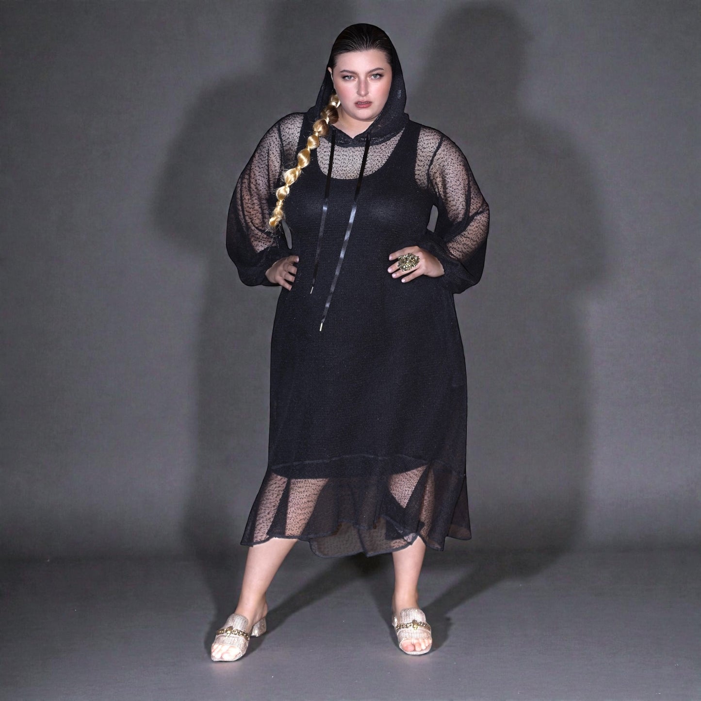 Plus Size Woman wearing a black dress with sheer overlay against a gray background.