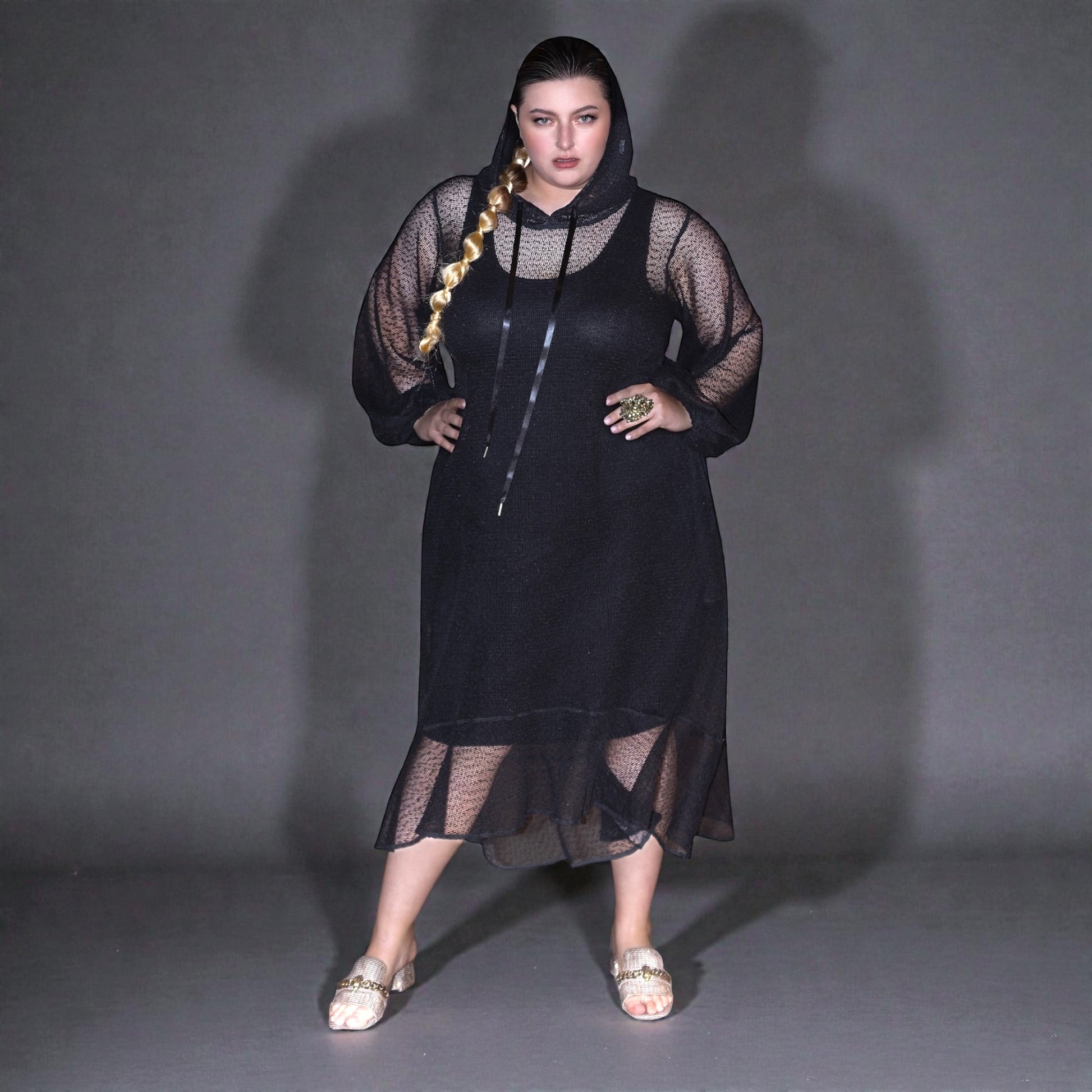 Plus Size Woman wearing a black dress with sheer overlay against a gray background.