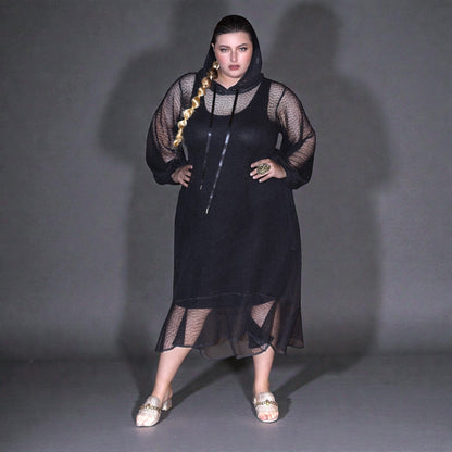 Plus Size Woman wearing a black dress with sheer overlay against a gray background.