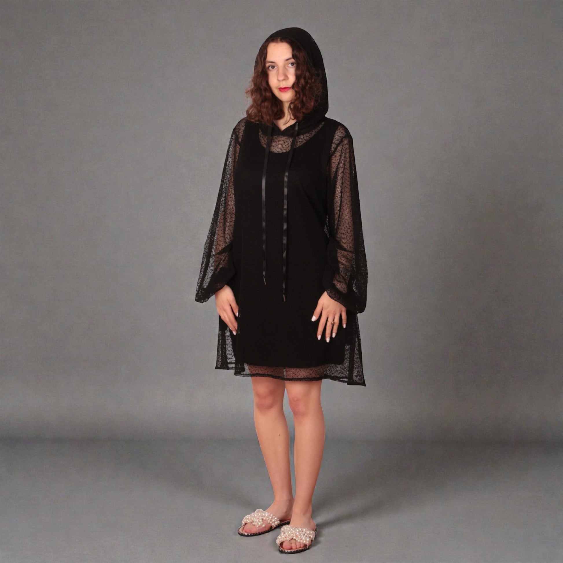 Woman wearing a black dress with sheer sleeves , hoodie and black undergarment against a white background