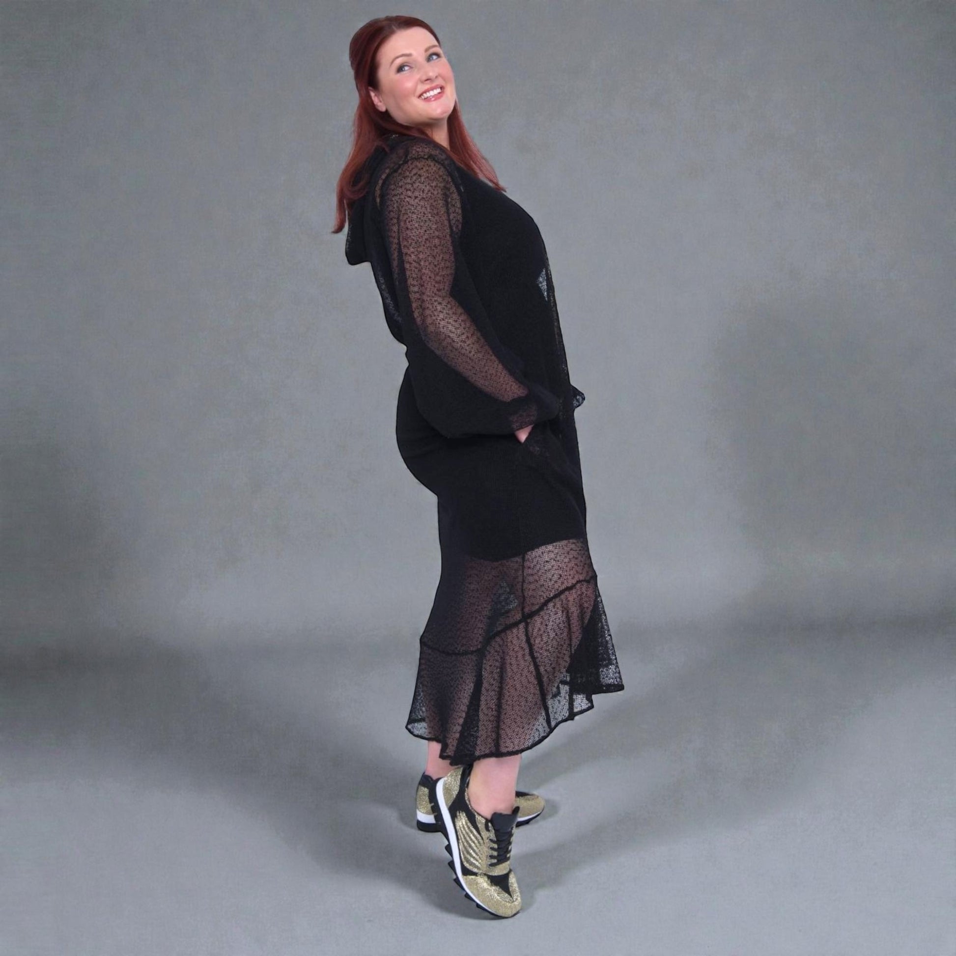 Plus Size Woman wearing a black dress with sheer overlay against a gray background.