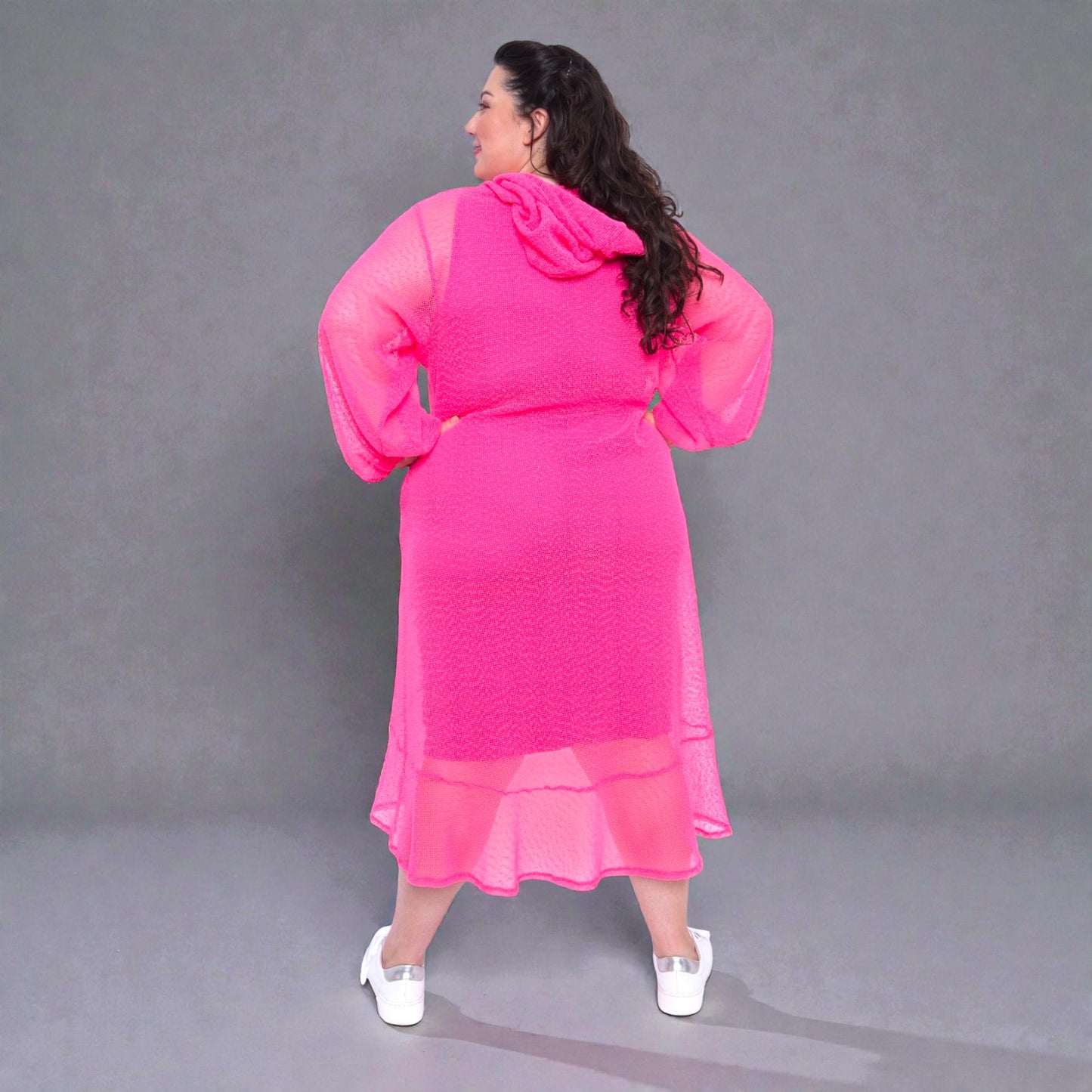 Women's Plus Size Aphrodite Hot Pink Holiday Resort Midi Dress with hoodie and hot pink undergarment, paired with white sneakers for a casual look.Grey Background.