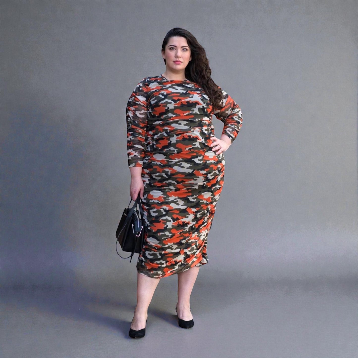 Plus Size Woman in an Orange Green Grey Camouflage Bodycon Midi Dress styled with  black heels for a modern, stylish look.Plain background.