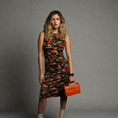Woman wearing a camouflage dress holding an orange clutch against a gray background