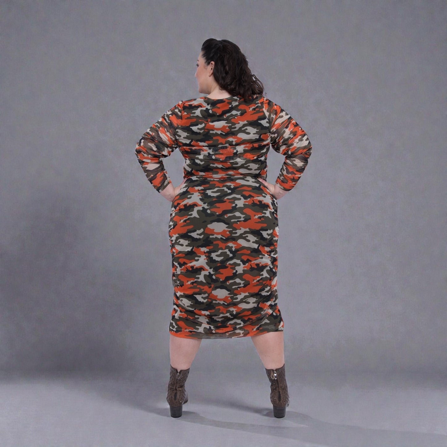 Plus Size Woman in an Orange Green Grey Camouflage Bodycon Midi Dress styled with green boots for a modern, stylish look.Plain background.