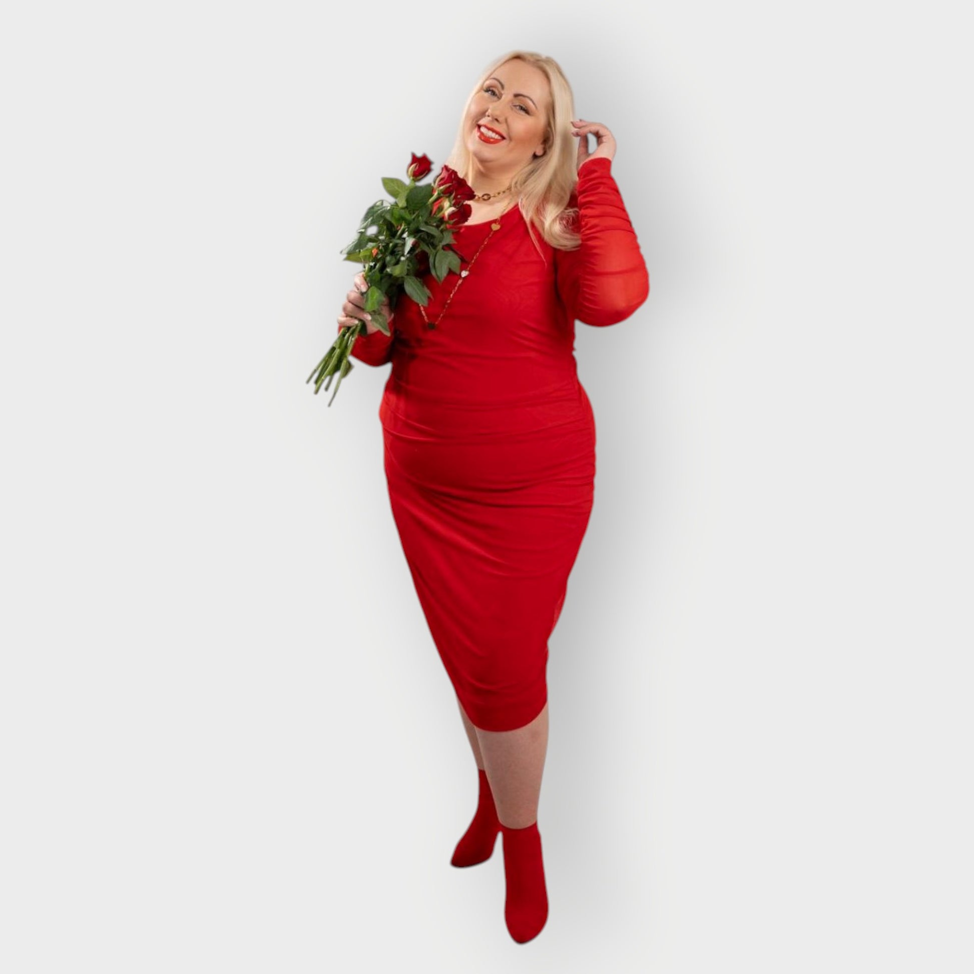 Women's Red Plus Size Boudicca Ruched Bodycon Midi Dress styled with gold jewelry and red heels, holding red roses for a romantic touch.