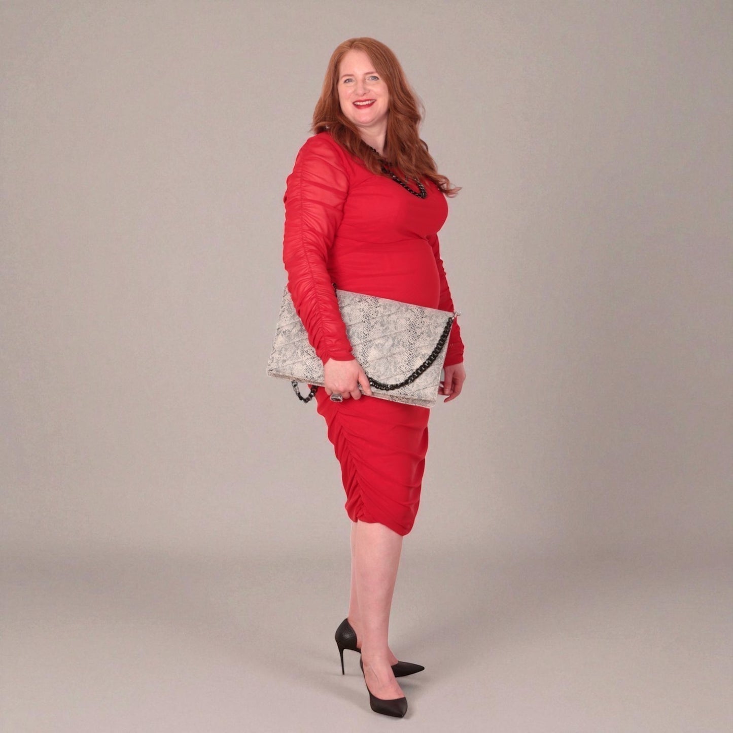 Woman in a red outfit holding a snakeskin quilted laptop clutch bag  against a white background