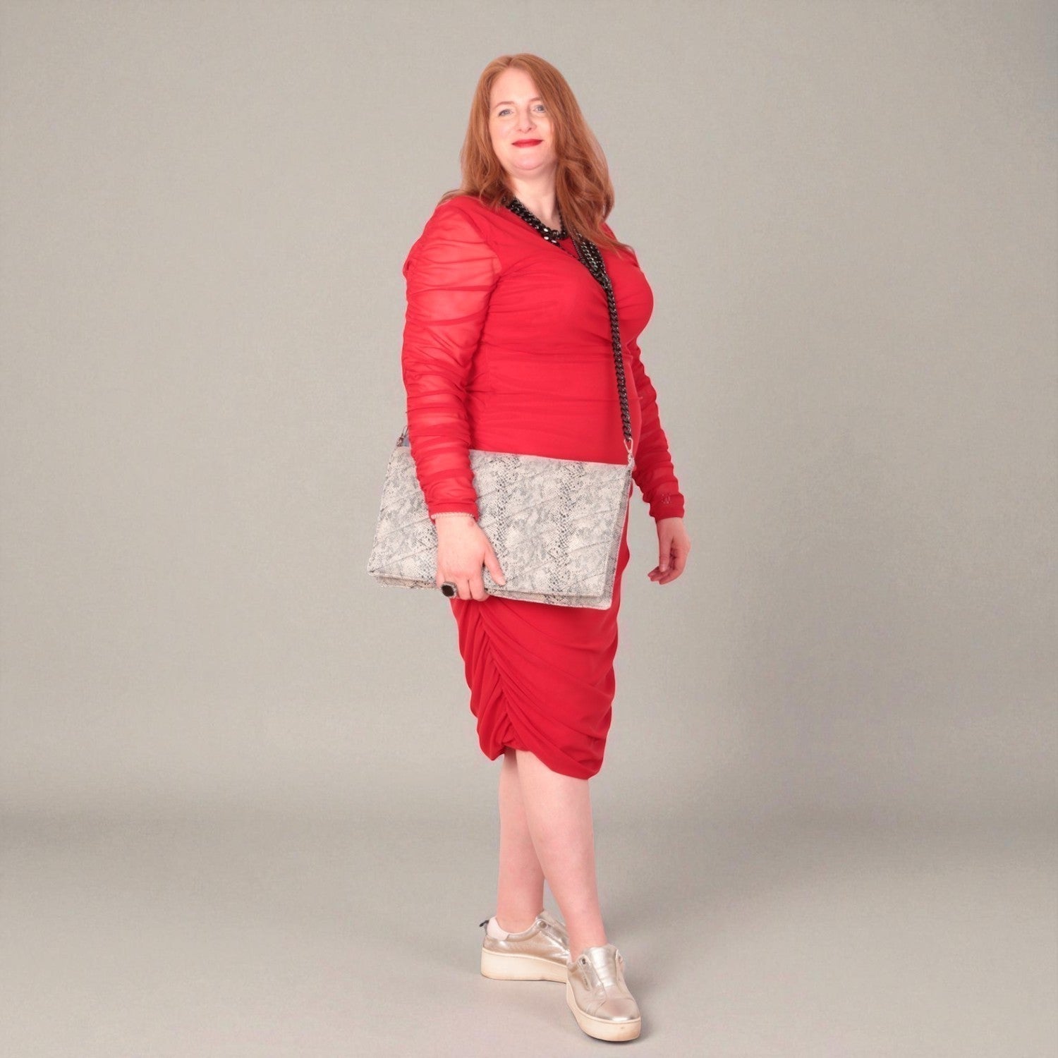 Woman in a red outfit holding a snakeskin quilted laptop clutch bag  against a white background