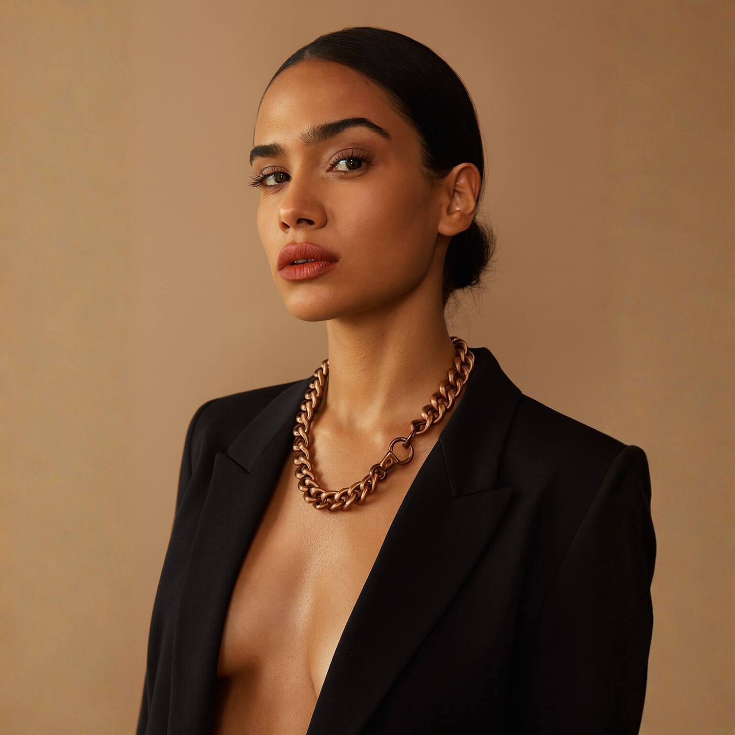 Woman wearing a black blazer and gold antique brass chain necklace against a beige background.