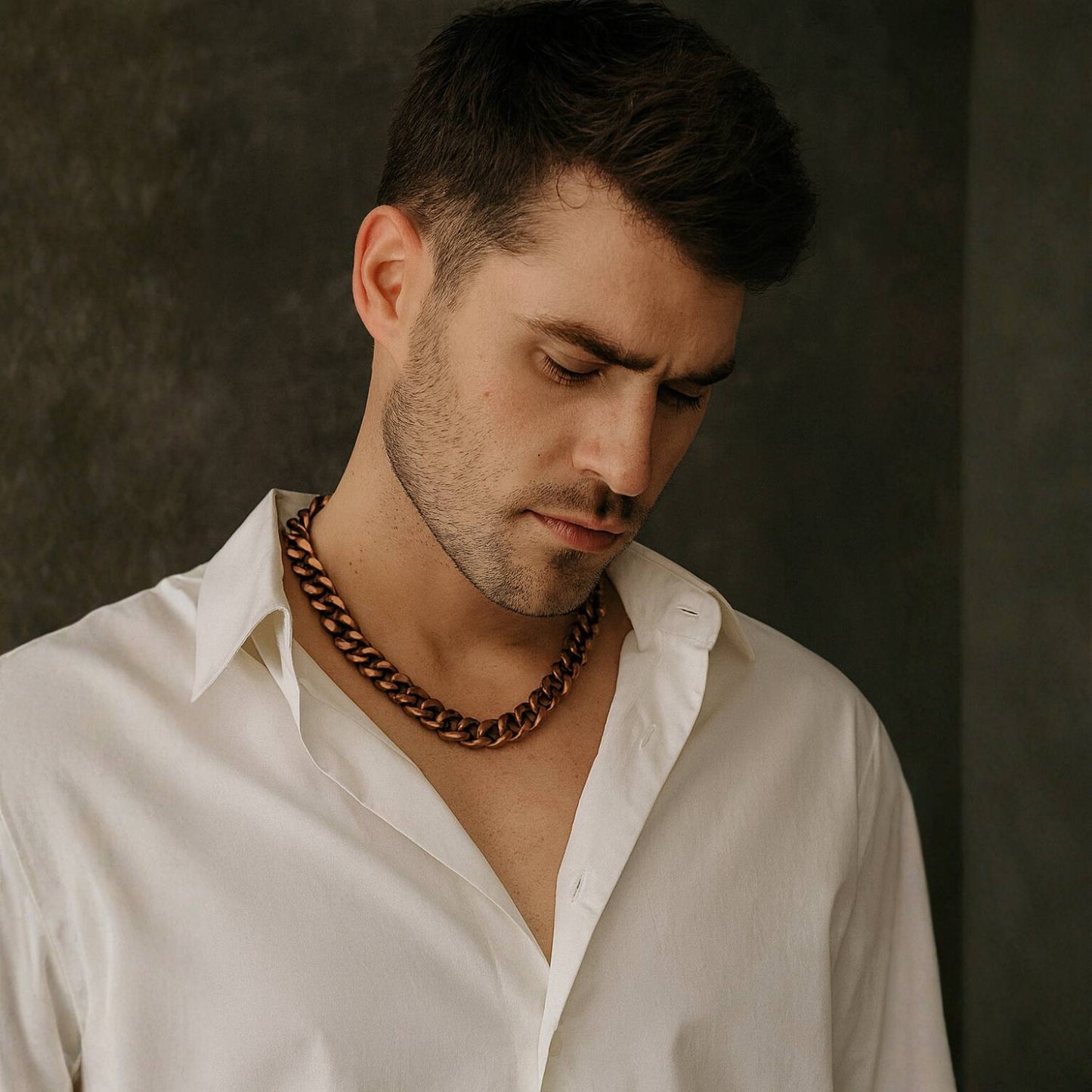 Man wearing a white shirt and a large gold antique brass necklace against a dark background