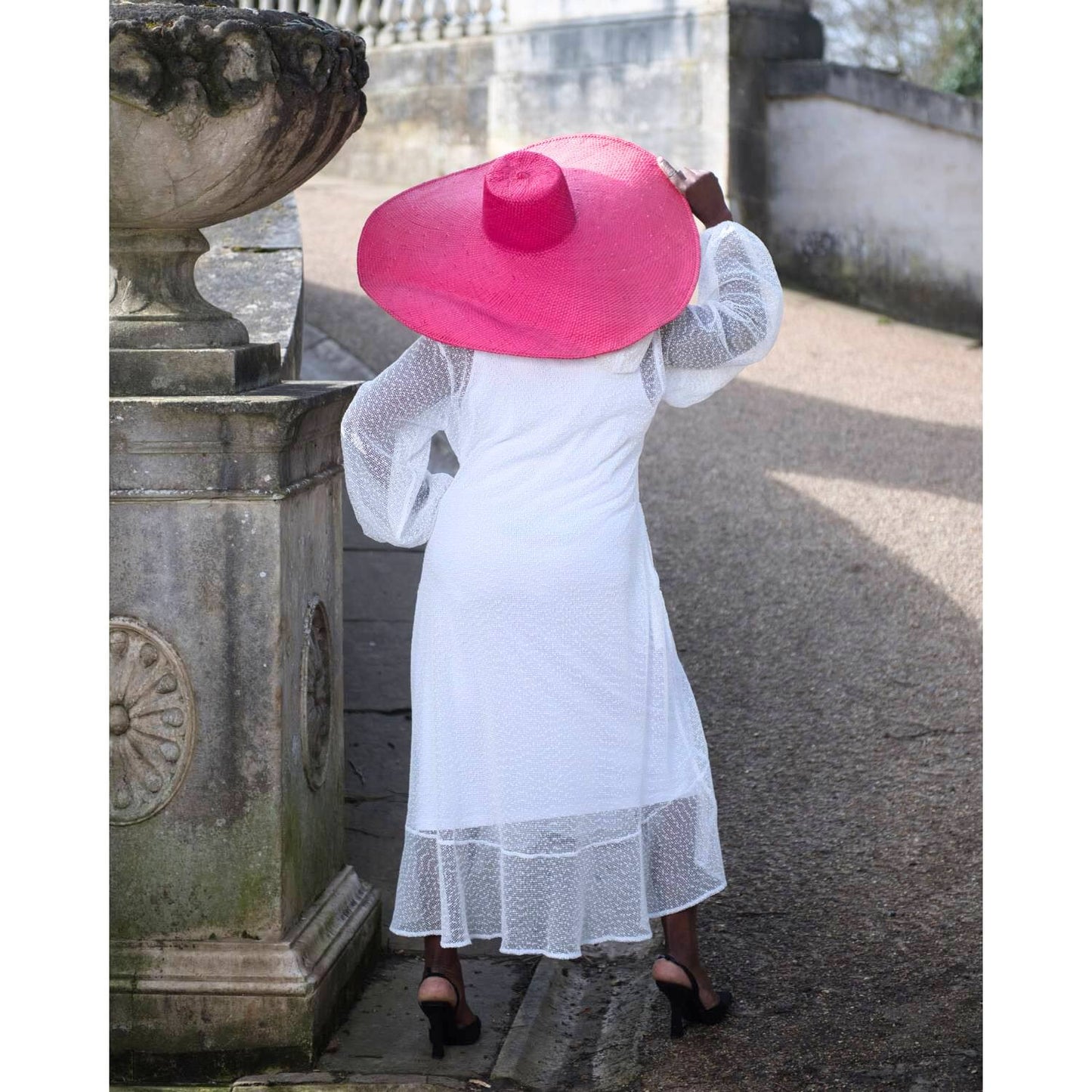 Women's Plus Size Aphrodite White Holiday Resort Dress with hoodie and white undergarment shown from the back, paired with a pink sunhat and black heels.