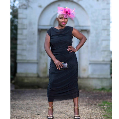Women's Boudicca Summer Black Ruched Bodycon dress styled with a pink hairpiece, black and gold clutch, and  gold chain black heels for a stylish look.
