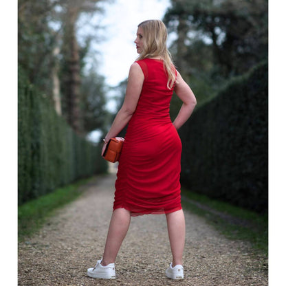 Women's Boudicca Summer Red Ruched Bodycon Midi Dress shown from the back, styled with an orange handbag and white sneakers for a chic, modern ensemble.