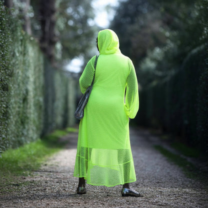 Women's Aphrodite Neon Lime Holiday Resort Dress with hoodie and matching neon lime undergarment shown from the back, styled with a silver  handbag and silver flats.