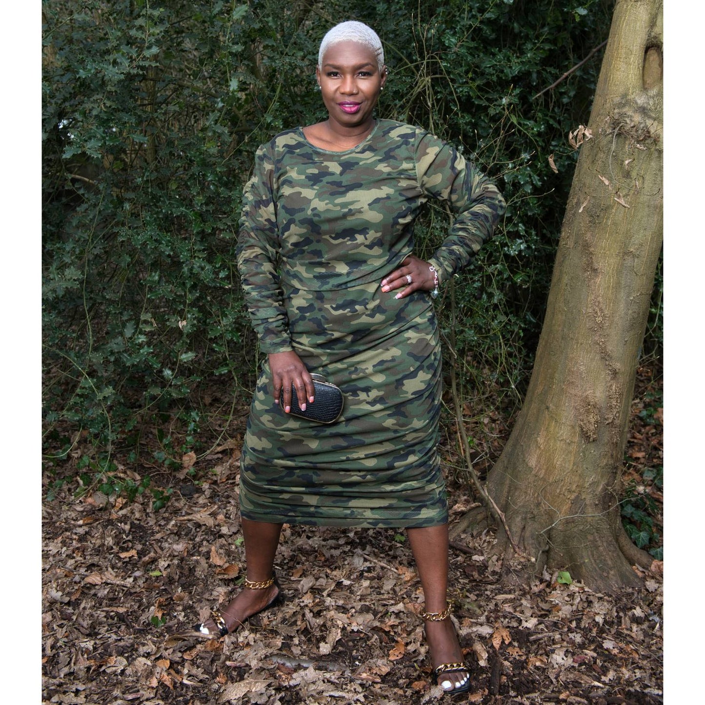 Women's Plus Size Olive Green Camouflage Bodycon Midi Dress styled with gold chain heels and a black and gold clutch for a sophisticated touch.