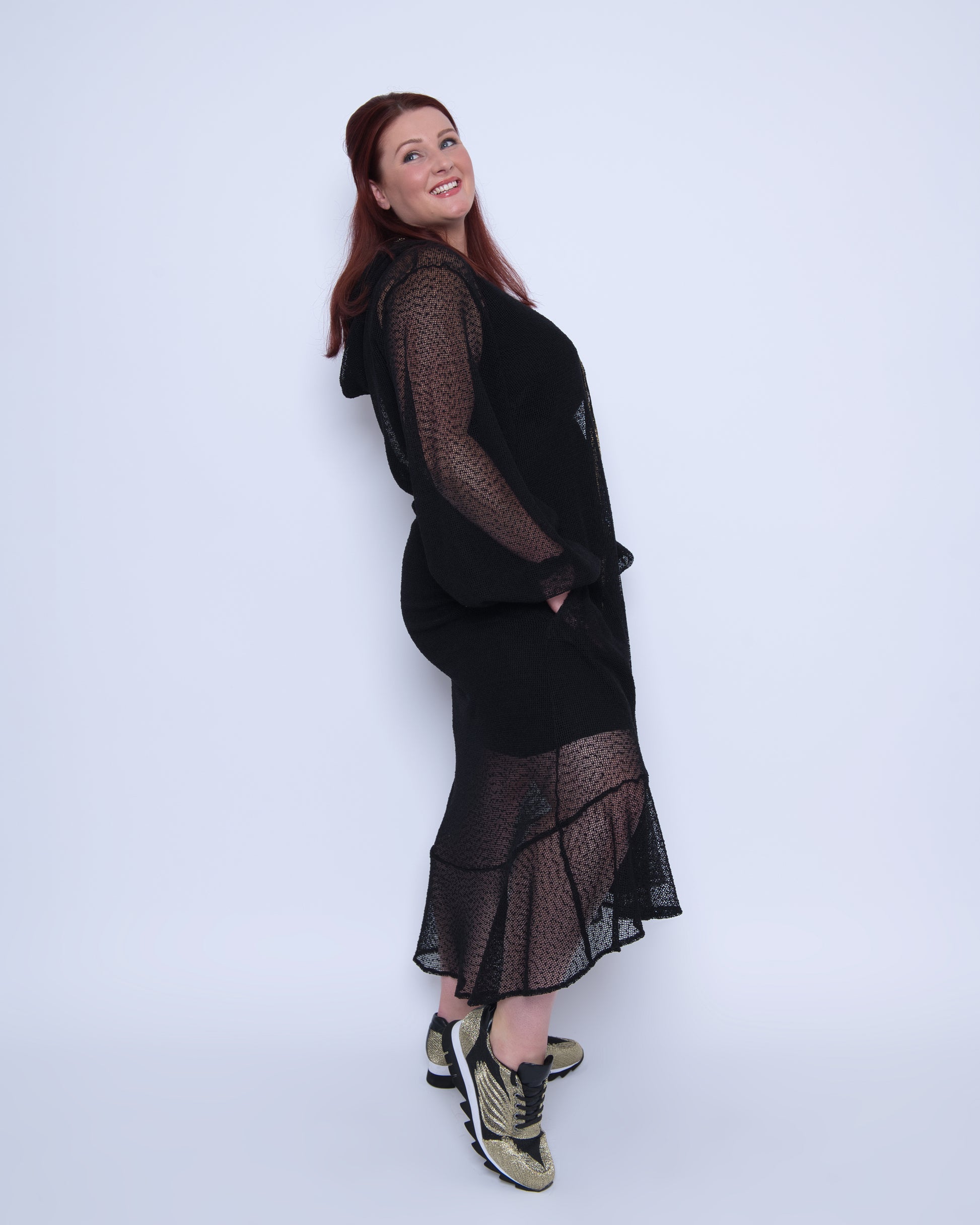Plus Size Aphrodite Black Holiday Resort Dress with hoodie and black undergarment shown from the side, paired with gold and black sneakers.