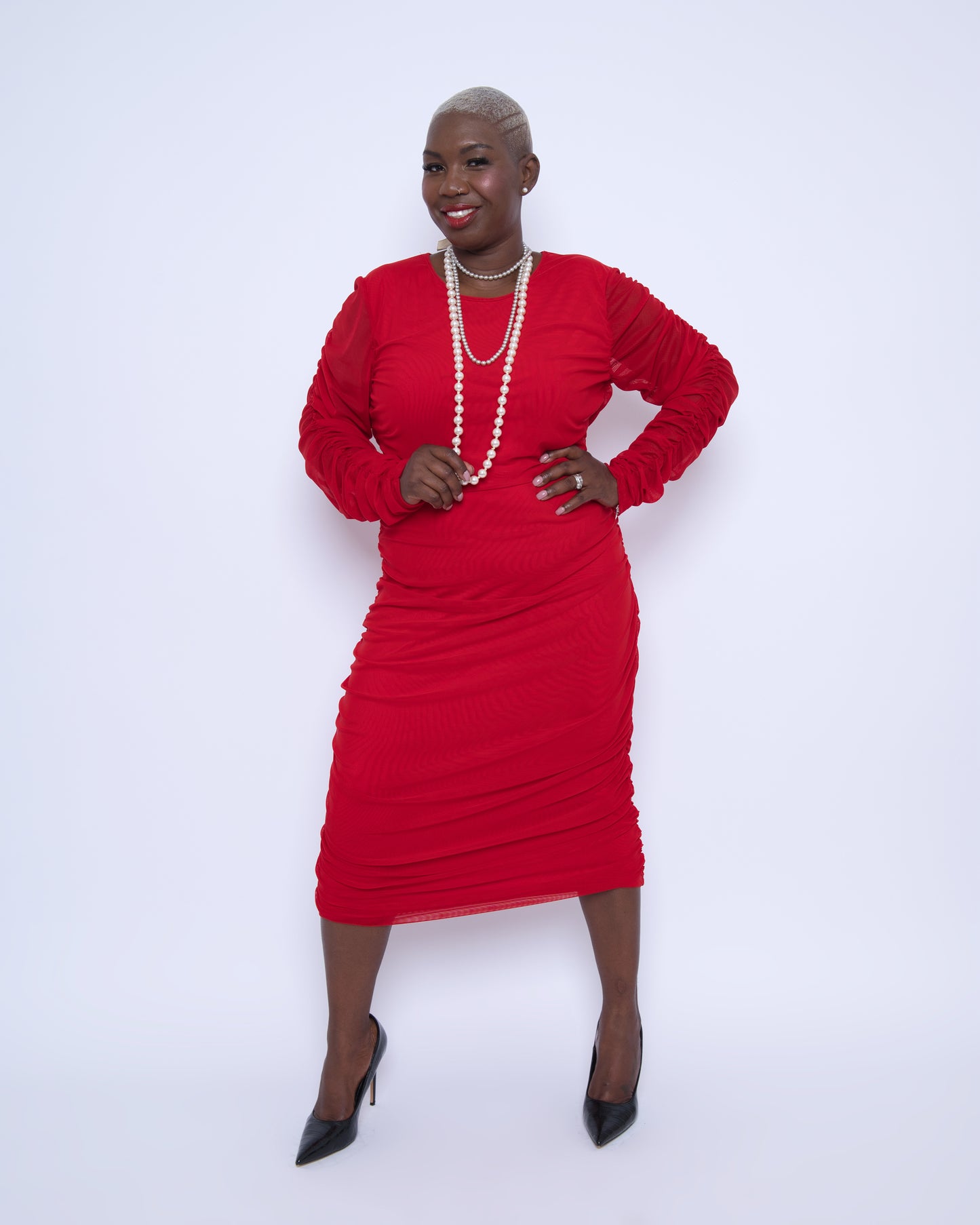 Women's Red Plus Size Boudicca Ruched Bodycon Midi Dress styled with pearl jewelry and black heels for a sophisticated, elegant ensemble.